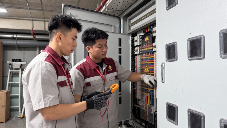 Hai nhân viên kỹ thuật M.O.R.E trao đổi tình trạng thiết bị tại phòng điện